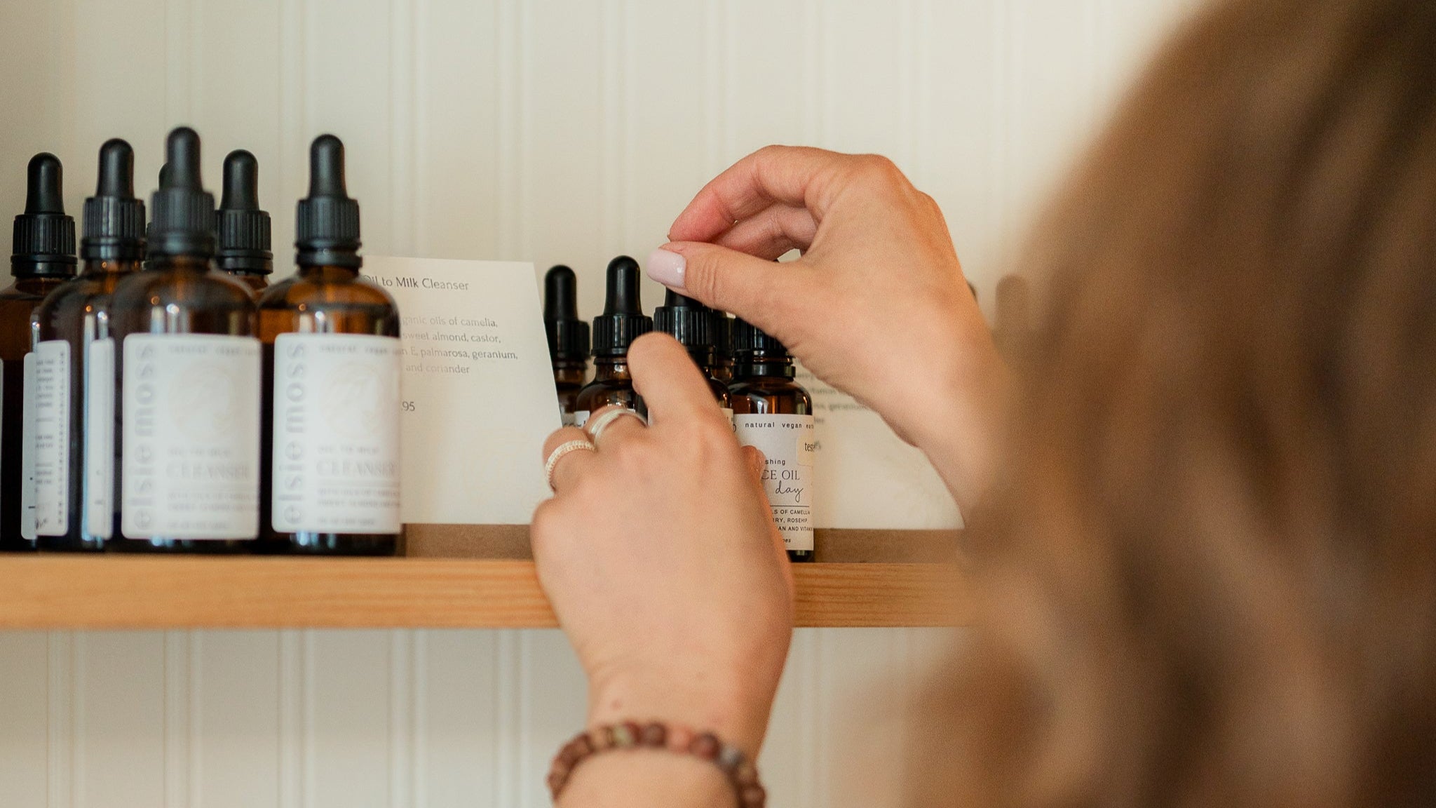 Person selecting a bottle from a shelf with various bottles and a candle in the background