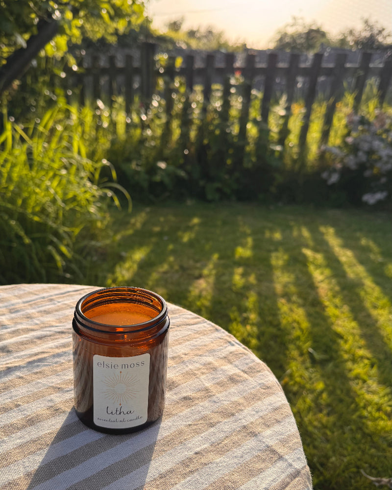 Candle in an amber glass jar on a striped surface with a garden background
