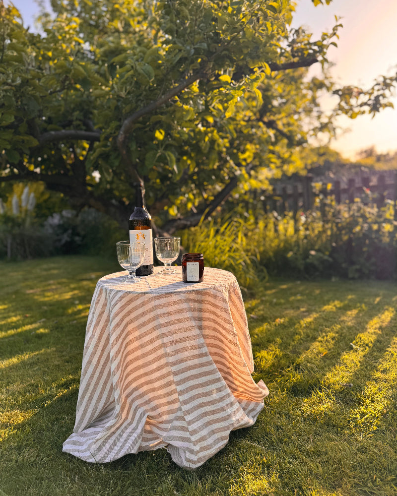 Table with wine bottle and glasses draped with a striped cloth in a garden setting