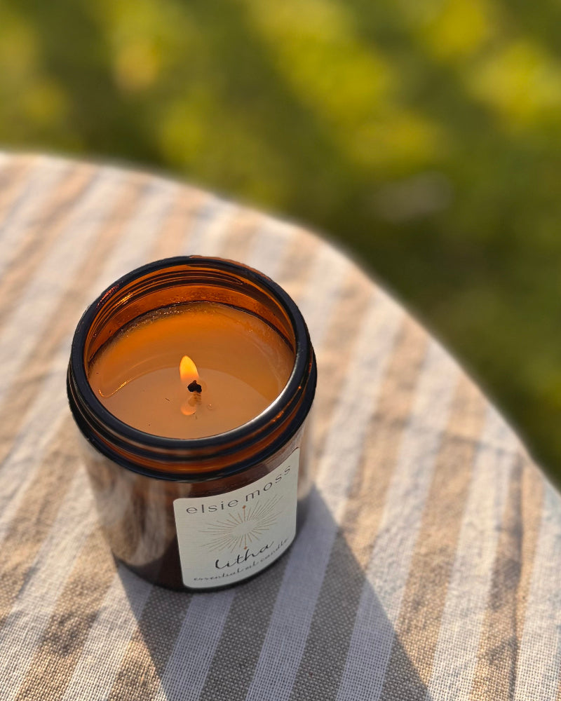 Lit candle in a glass jar on a wooden surface with a blurred green background
