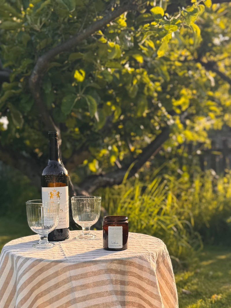 Wine bottle, glasses, and candle on a table outdoors with trees in the background