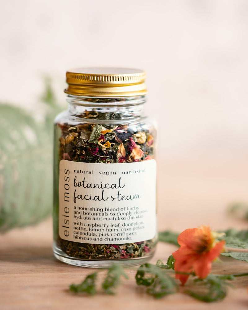 Jar of botanical facial steam with a gold lid on a wooden surface with flowers and leaves.