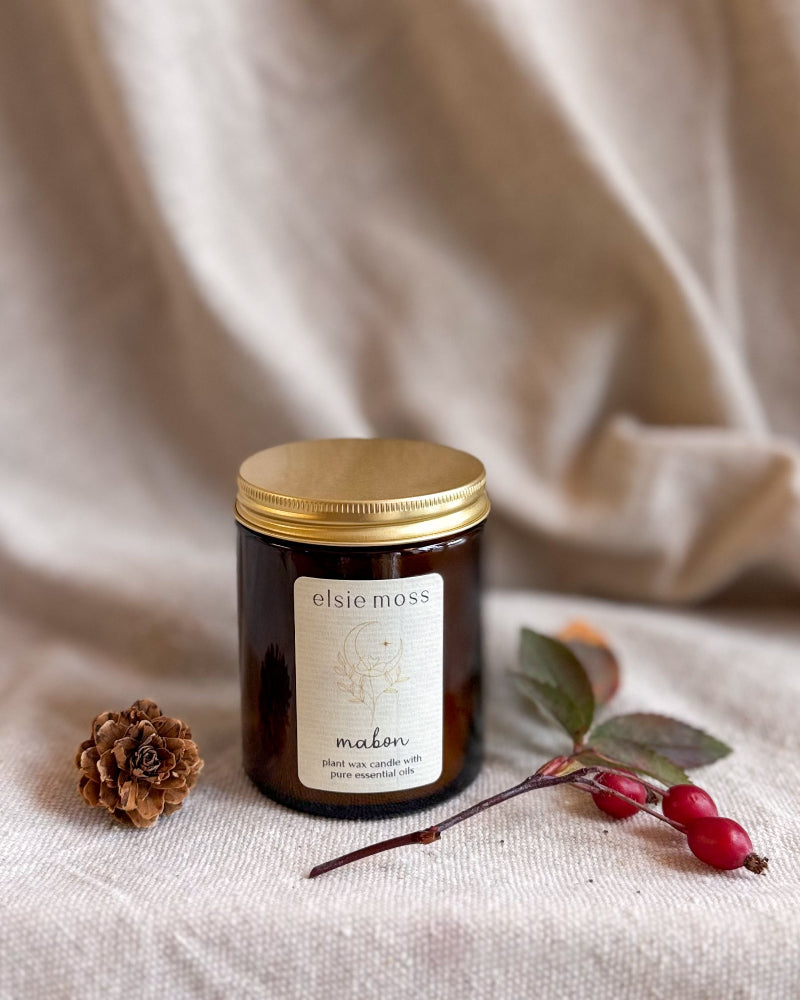 A dark amber glass jar candle with a gold lid and a cream label reading &