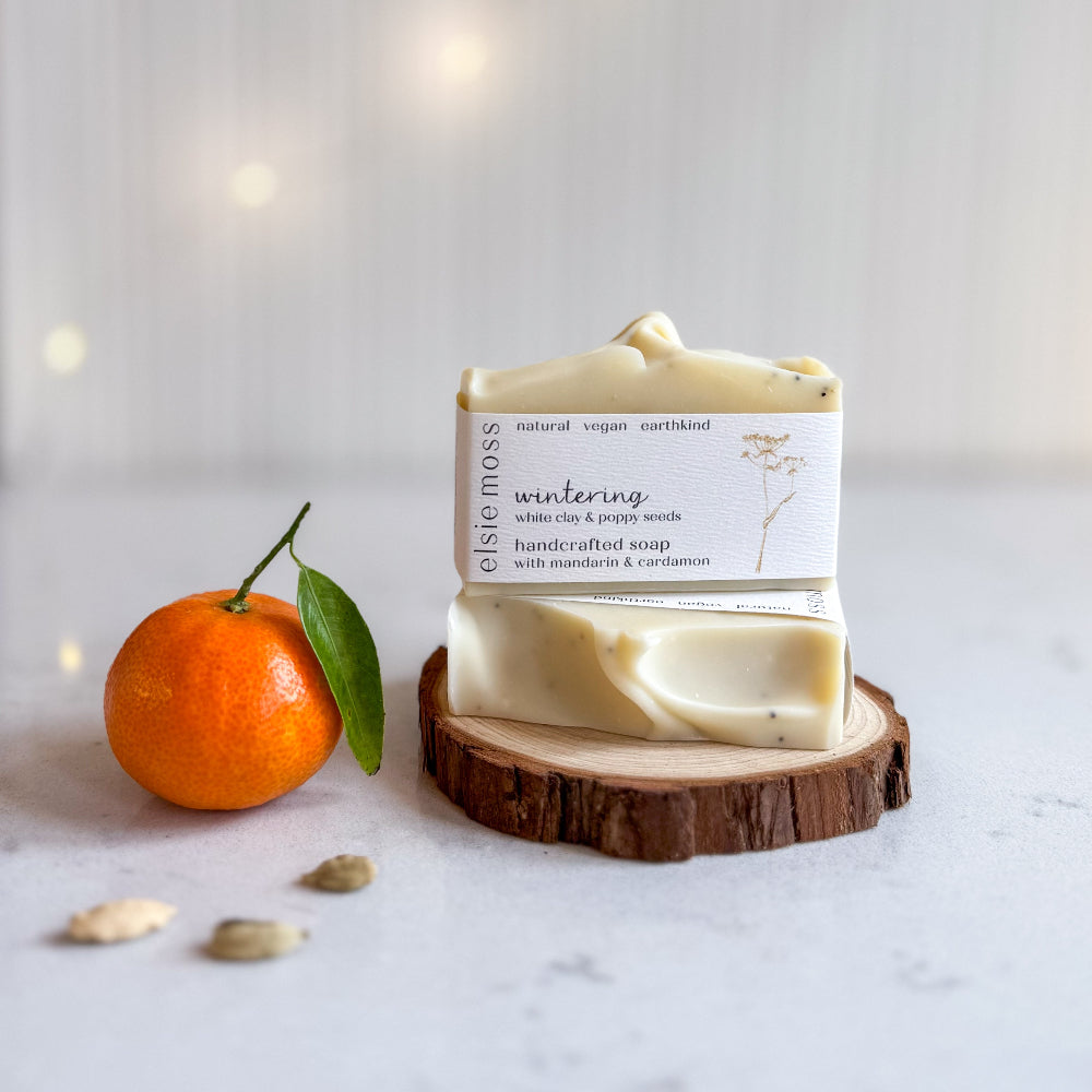 Bar of soap on a wooden stand with an orange and leaves on a light background
