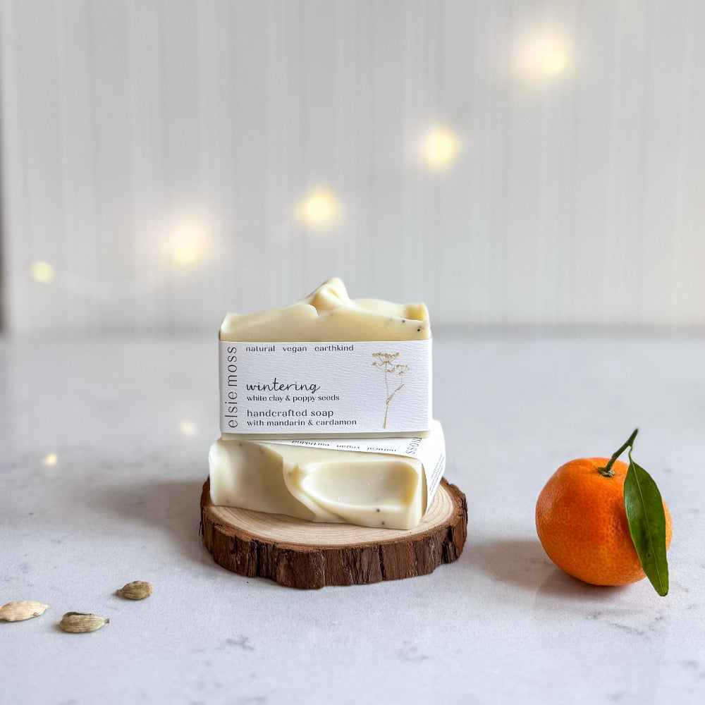 Bar of soap on a wooden stand with an orange and leaves on a light background