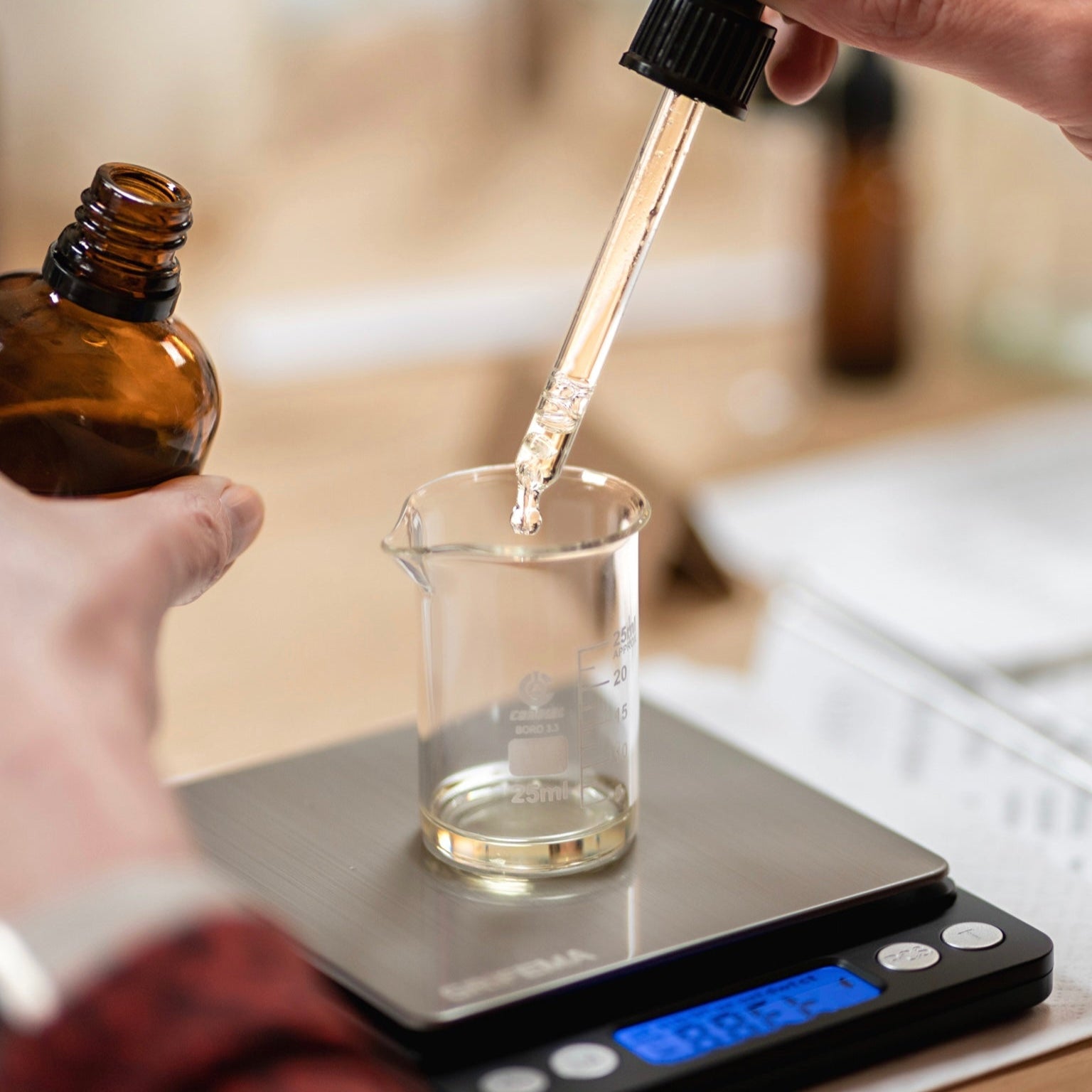 person using a dropper to add oils to a glass vessel
