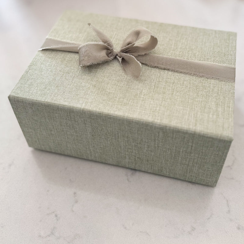 Green gift box with a ribbon on a light marble surface