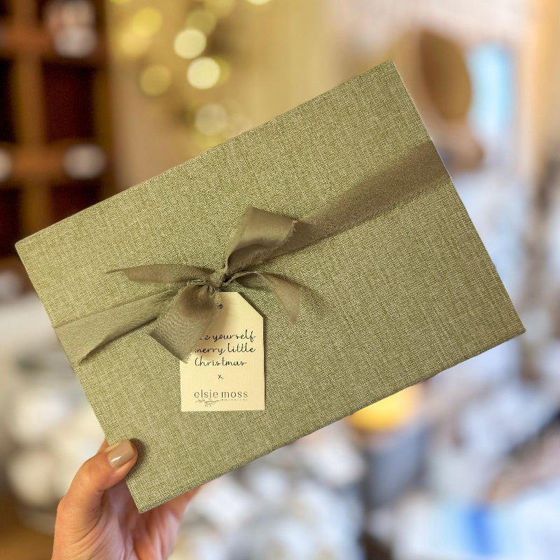Green gift box with a ribbon and tag held by a hand against a blurred background