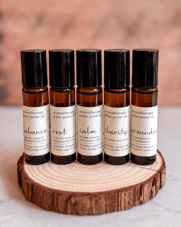 Set of five aromatherapy pulse point oil bottles on a wooden stand with a blurred background.