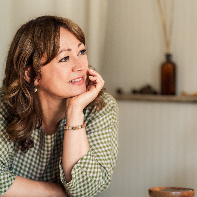 Woman in a green checkered shirt sitting indoors with a neutral background