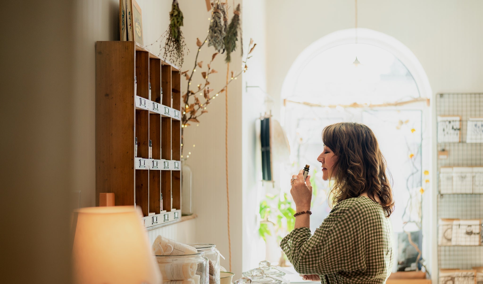 Woman smelling aromatherapy products in a well-lit shop with bath and body products.