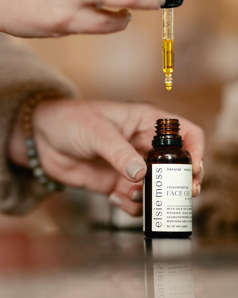 Person using a dropper to apply Elsie &amp; Moss face oil on a blurred background