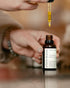 Person using a dropper to apply Elsie & Moss face oil on a blurred background