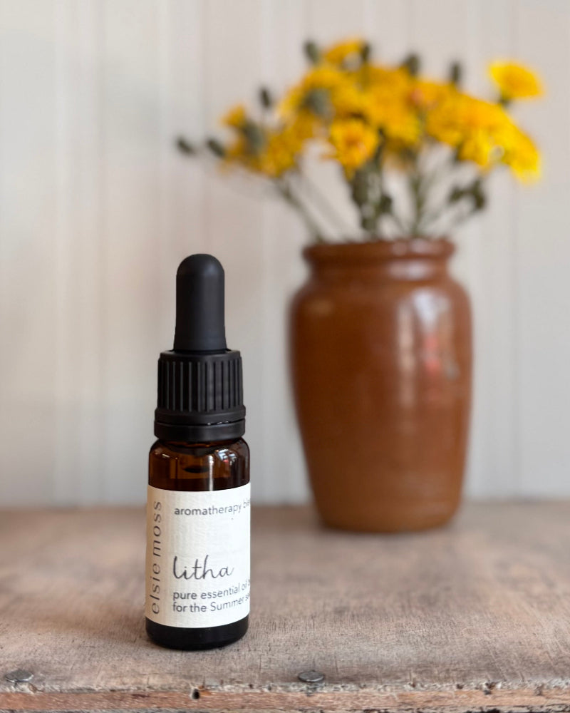 Bottle of essential oil with a dropper on a wooden surface, featuring a vase with yellow flowers in the background.