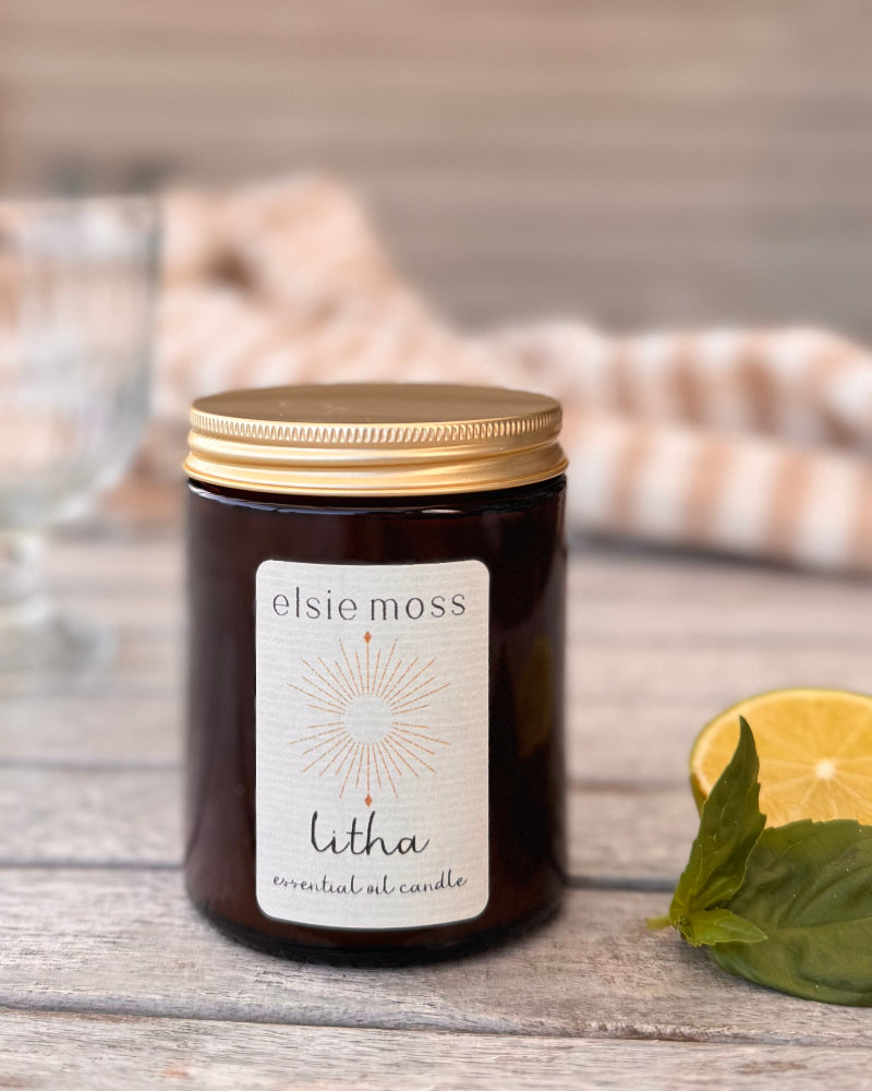 Elsie Moss Litha candle on a wooden surface with a lemon and leaves.