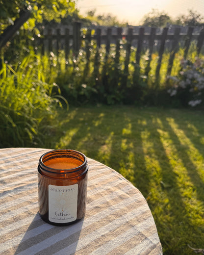 Candle in an amber glass jar on a striped surface with a garden background