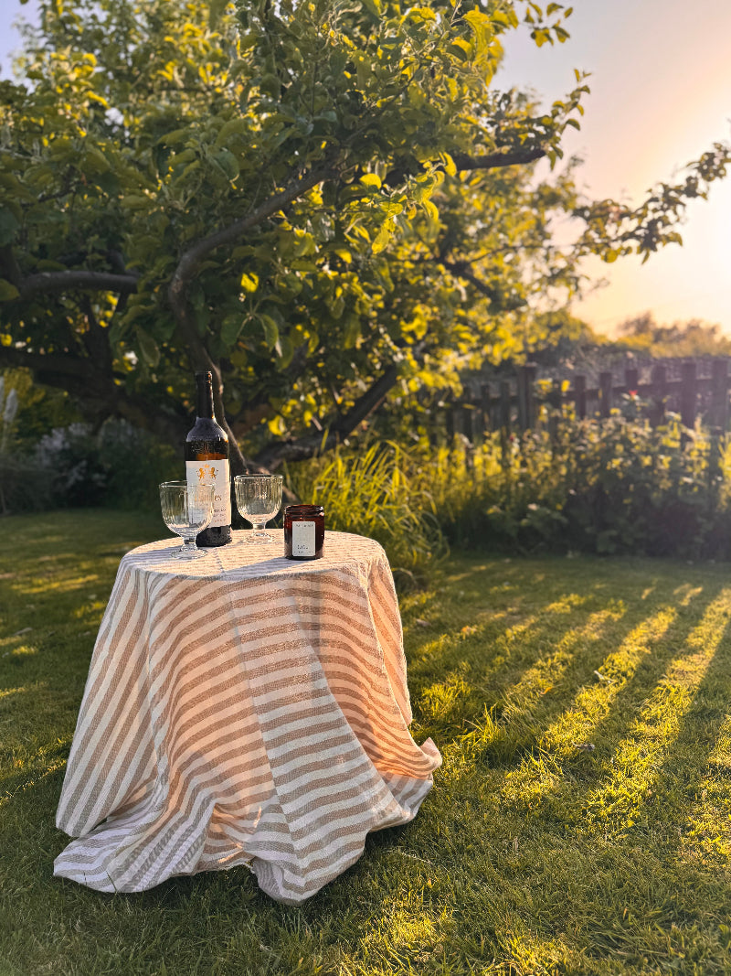 Table with wine bottles and glasses under a tree in a garden setting