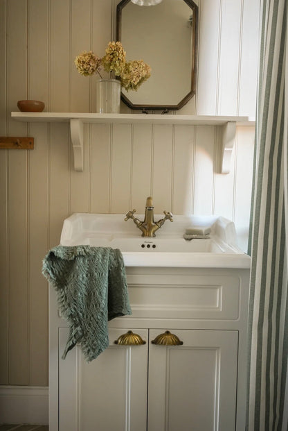 Bathroom vanity with white sink, gold faucet, and green towel.