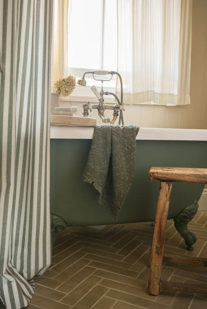 Vintage-style bathroom with a green bathtub, wooden stool, and striped shower curtain.