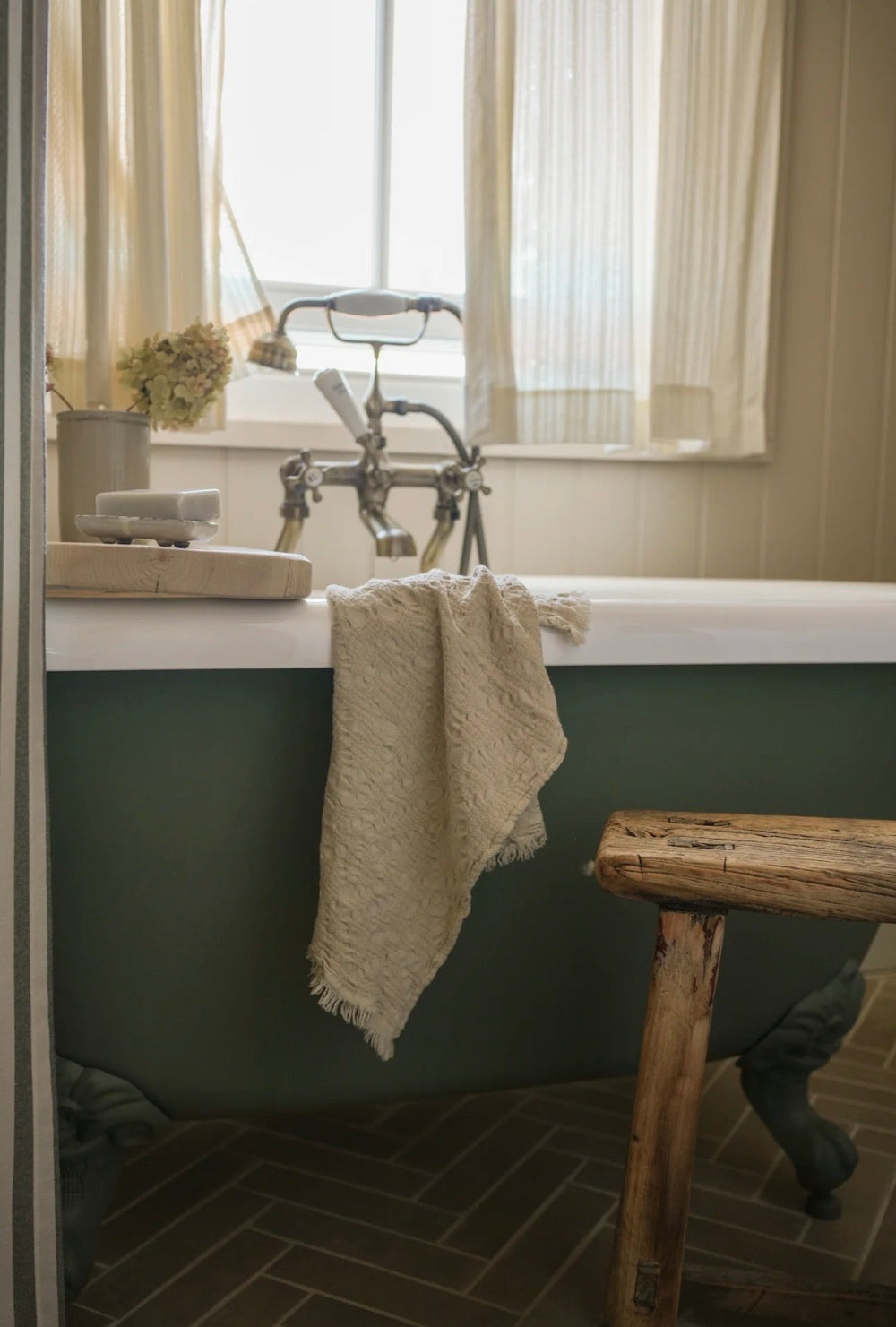 Bathroom with a green bathtub, wooden stool, and towel hanging over the edge.