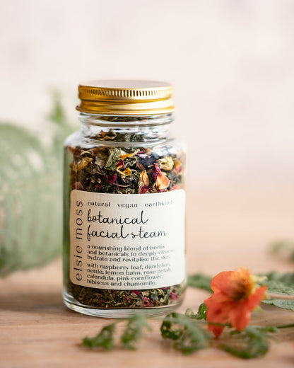 Jar of botanical facial steam with a gold lid on a wooden surface with flowers and leaves.