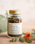 Jar of botanical facial steam with a gold lid on a wooden surface with flowers and leaves.