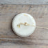 Round white shampoo bar with a small sprig on a wooden surface