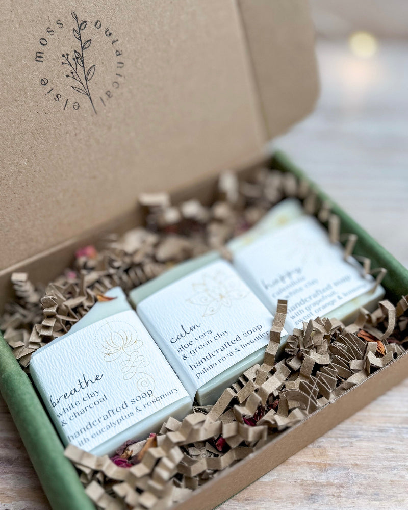 Three soaps in a decorative box with text on a wooden surface