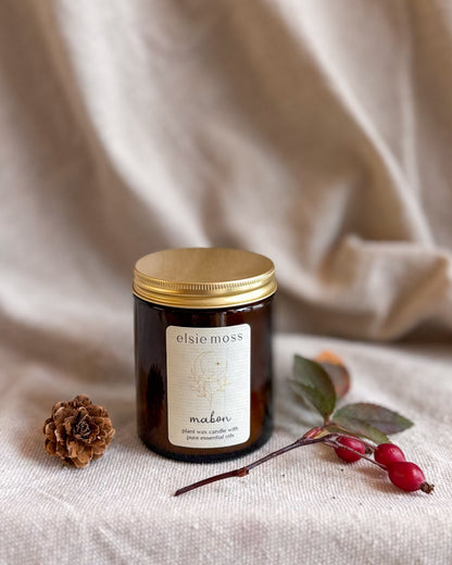 A dark amber glass jar candle with a gold lid and a cream label reading &