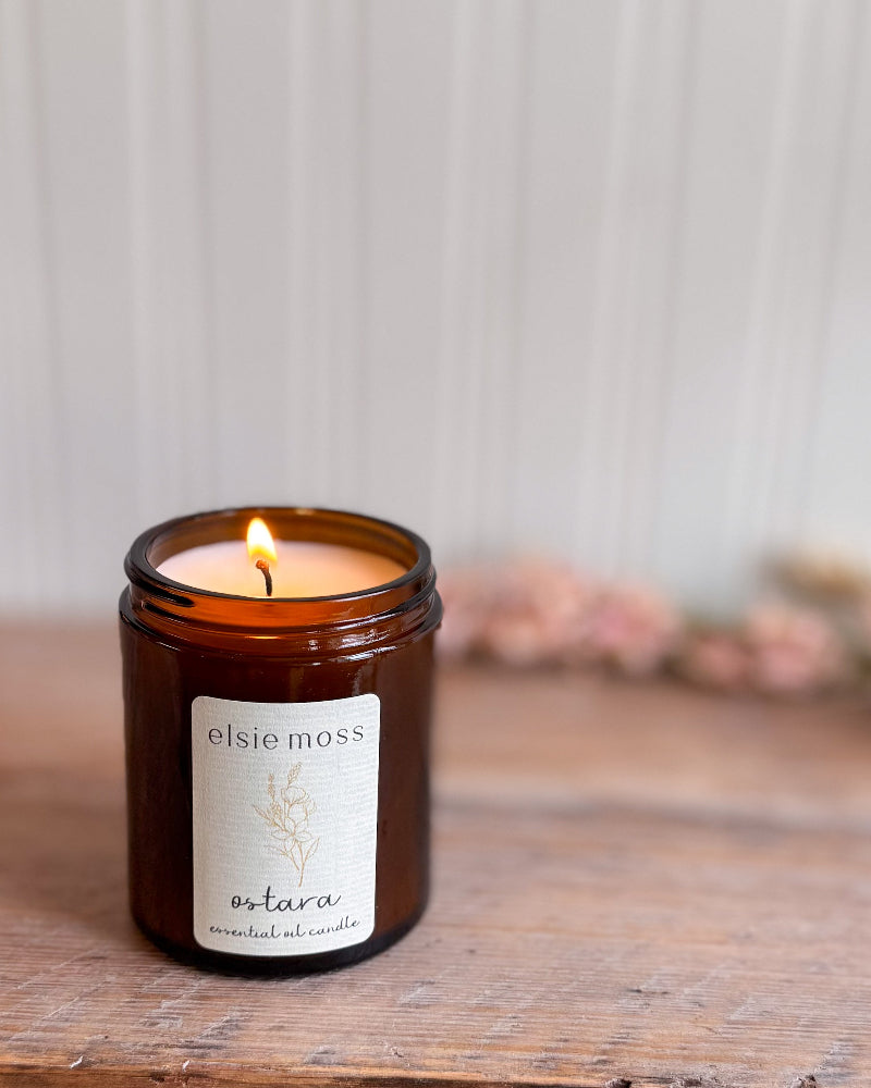 Elsie Moss candle in a glass jar on a wooden surface with a blurred background