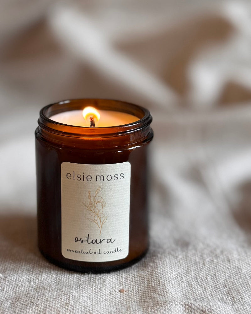 Elsie Moss Ostara essential oil candle in a brown glass jar on a textured surface.