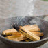 Palo santo sticks burning in a dark bowl with smoke rising.