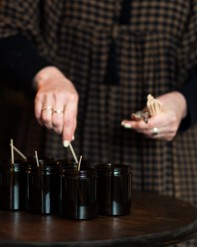 Person lighting small candles in black jars on a wooden table.