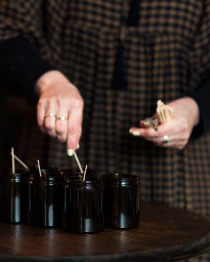 Person lighting small candles in black jars on a wooden table.