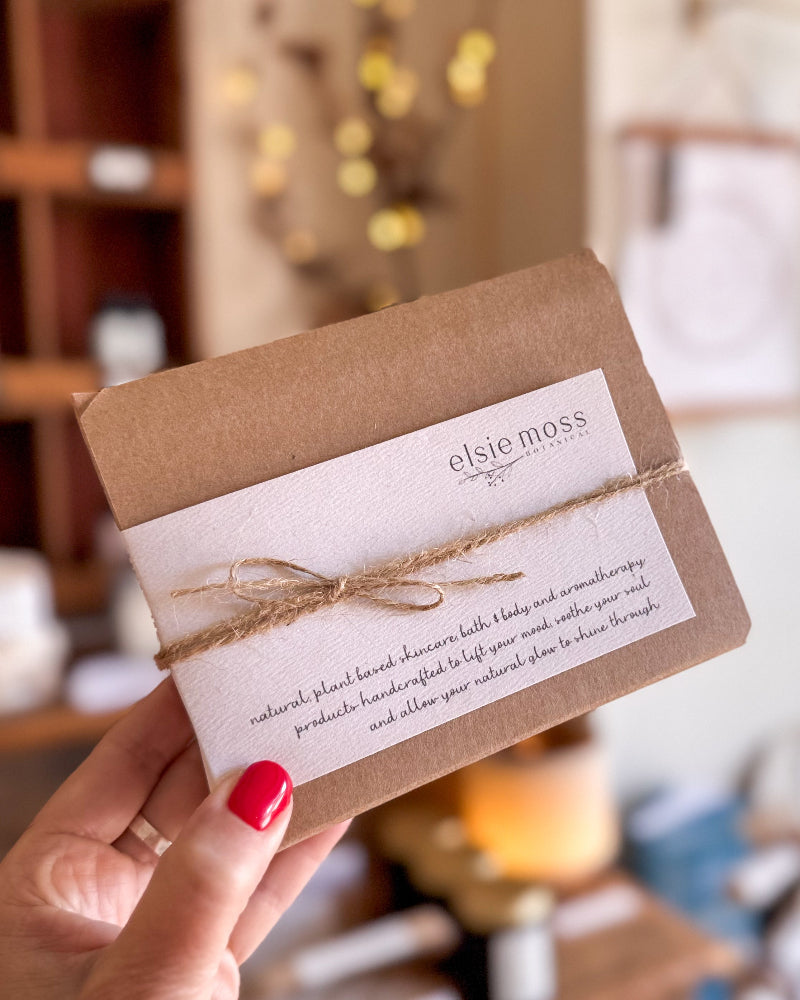 A hand with red nail polish holds a small kraft paper envelope with a white label reading &