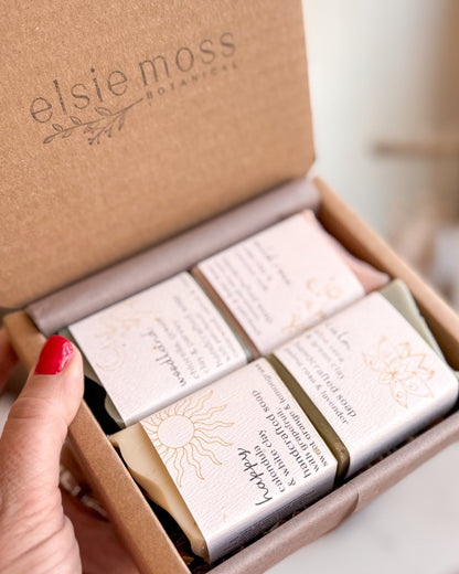 A hand with red nail polish holds an open kraft paper box labeled &