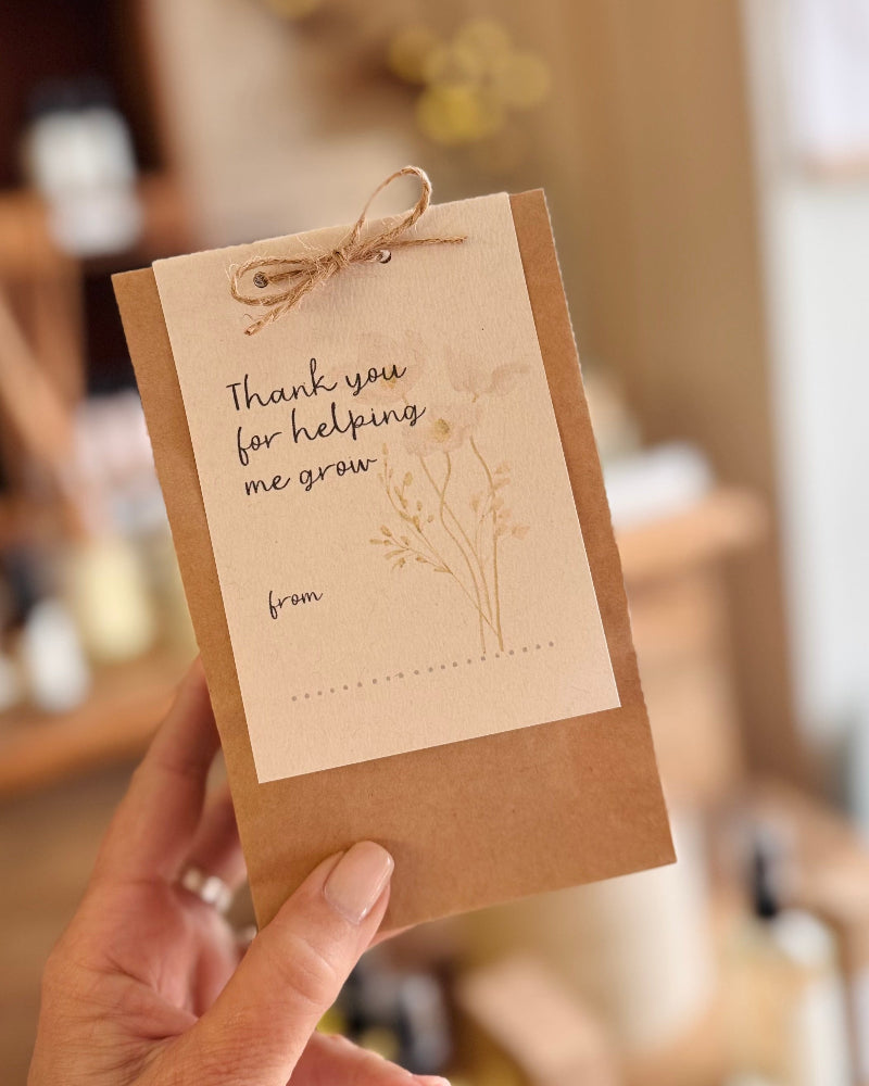 A hand holding a kraft paper envelope with a printed thank-you card attached. The card reads &