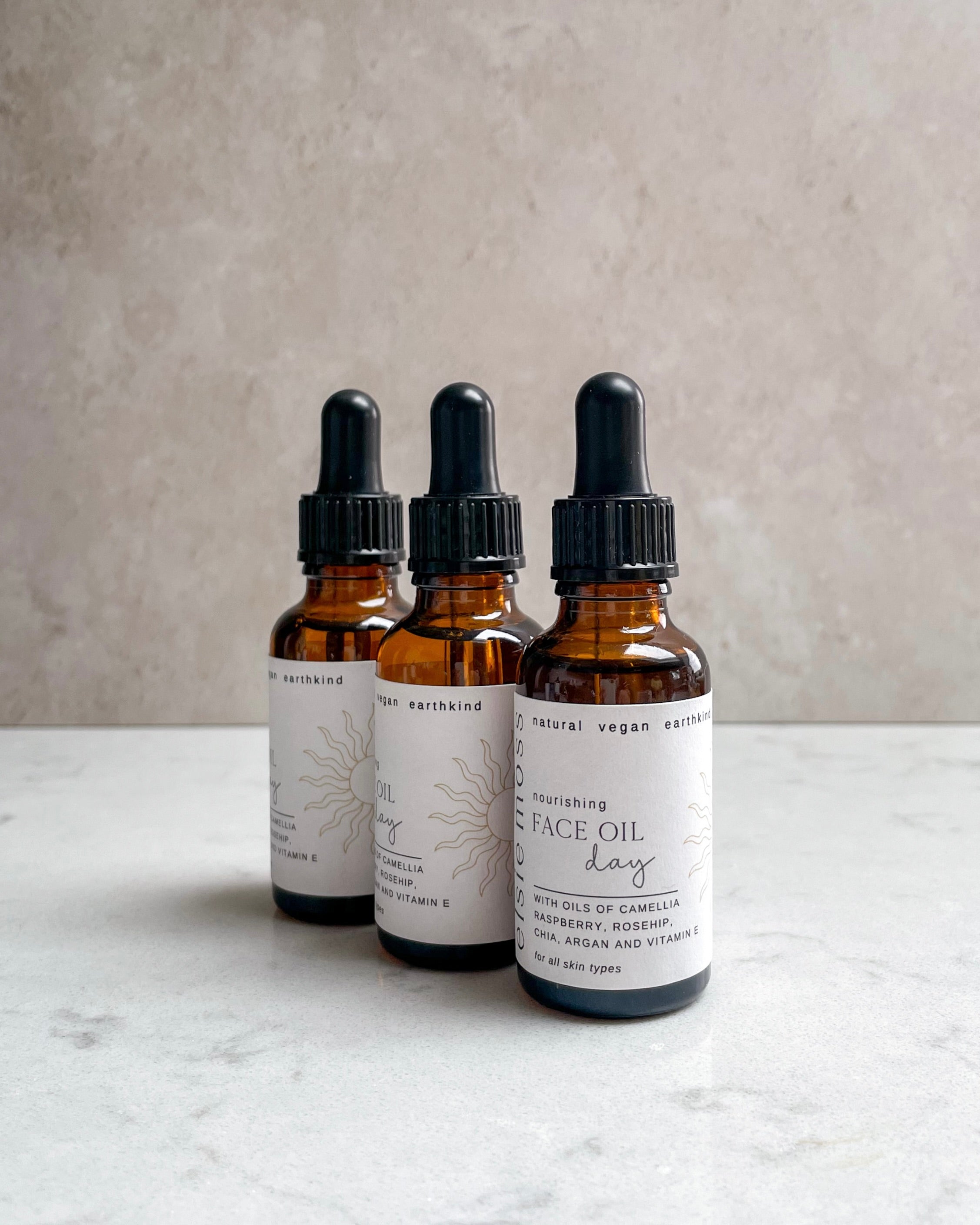 Three bottles of facial oil with droppers on a marble surface.