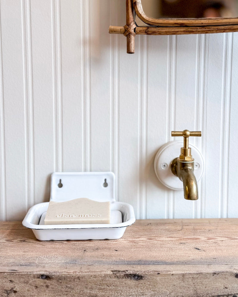 Bathroom setting with a wooden counter, white soap dish, and gold faucet against a white paneled wall.